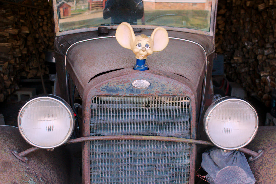 Rustic old car with a cheerful mouse hood ornament parked indoors.