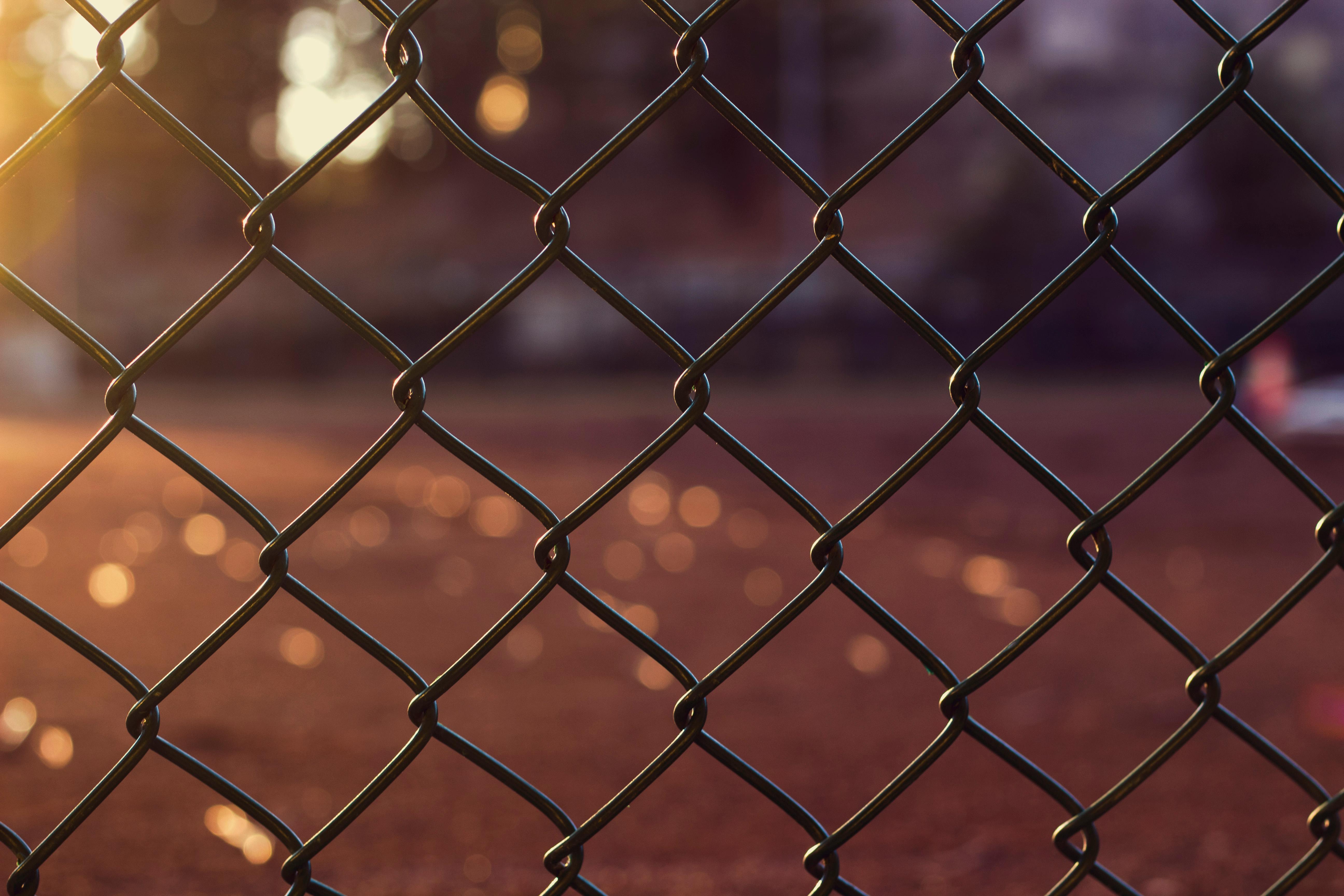 Close-up of a chain link fence with warm sunlight and soft bokeh, representing metallnetting mot rotter